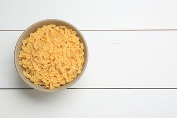 Raw farfalline pasta in bowl on white wooden table, top view. Space for text