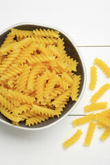 Raw fusilli pasta in bowl on white wooden table, top view