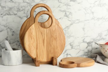 Wooden cutting boards and mortar with pestle on white table near marble wall