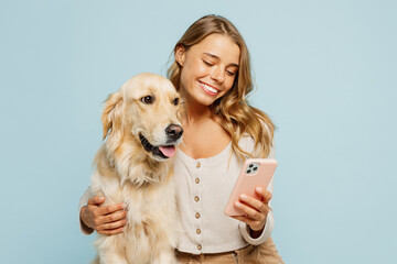 Young smiling fun owner woman with her best friend retriever wear casual clothes hold use mobile cell phone hug dog isolated on plain pastel light blue background studio. Take care about pet concept.