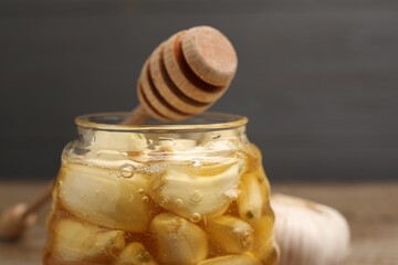 Honey with garlic in glass jar and dipper on blurred background, closeup. Space for text