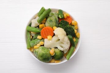 Mix of different frozen vegetables in bowl on white wooden table, top view