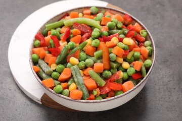 Mix of different frozen vegetables in bowl on grey table, closeup