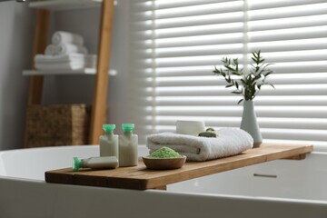 Wooden tray with spa products and green branches on bath tub in bathroom