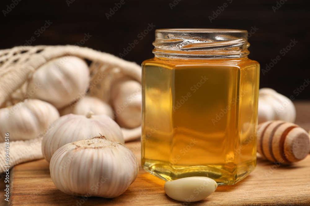 Wall mural Jar with honey, garlic and dipper on wooden board, closeup