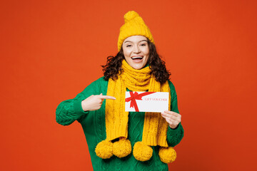 Young surprised happy woman wear green knitted sweater yellow hat scarf hold point on gift...