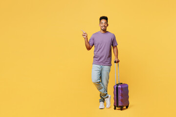 Traveler happy man wears casual clothes hold bag point finger aside isolated on plain yellow background studio. Tourist travel abroad in free spare time rest getaway. Air flight trip journey concept. - obrazy, fototapety, plakaty