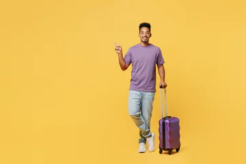 Foto op Aluminium Traveler happy man wears casual clothes hold bag point finger aside isolated on plain yellow background studio. Tourist travel abroad in free spare time rest getaway. Air flight trip journey concept. © ViDi Studio