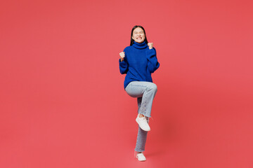 Full body young woman of Asian ethnicity she wear blue sweater casual clothes doing winner gesture celebrate clenching fists say yes isolated on plain pastel pink background studio. Lifestyle concept.