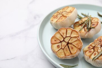 Heads of fried garlic and rosemary on white table, closeup. Space for text