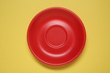 One red ceramic plate on yellow background, top view