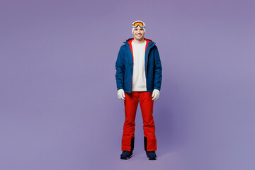 Full body smiling cheerful happy skier man wear warm blue windbreaker jacket ski goggles mask hat looking camera spend extreme weekend winter season in mountains isolated on plain purple background. © ViDi Studio