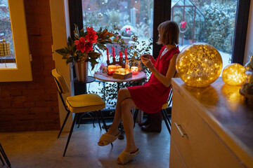 Woman sits by the table at beautifully decorated house for a winter holidays. Concept of coziness...