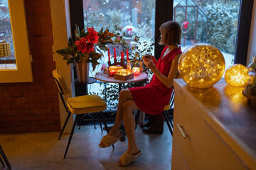 Woman sits by the table at beautifully decorated house for a winter holidays. Concept of coziness...