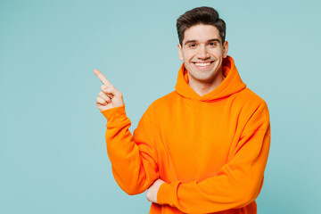 Young smiling happy fun man he wears orange hoody casual clothes point index finger aside on area...