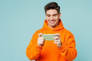 Young gambling man he wearing orange hoody casual clothes use play racing app on mobile cell phone...