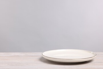 Empty ceramic plate on wooden table against light background, space for text