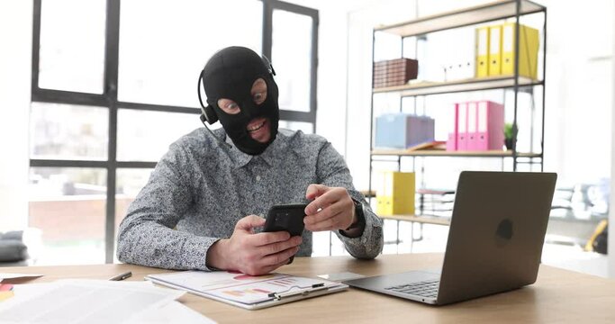 In the office, a scammer in a mask is talking on the phone, a close-up. Fraud circuit by phone, front view