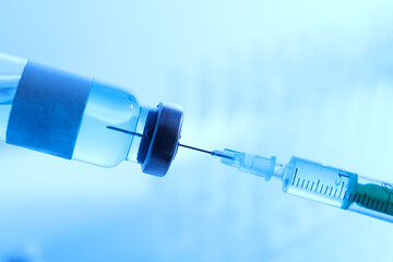 Glass bottle with vaccine and syringe on blue background, close up