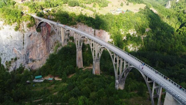 Aerial drone view of arched Djurdjevica Bridge with moving cars over Tara river canyon in Montenegro, green landscape in summer. Popular tourist destination near Zabljak town in Durmitor National Park