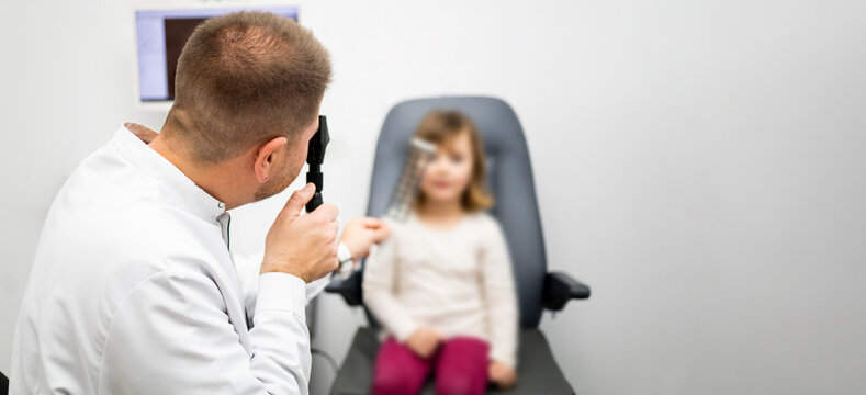 An unrecognizable ophthalmologist uses a retinoscopy ruler on a young girl to view the pupillary shadow to determine the degree of refractive eye refraction. Concept of retinoscopy in young children.