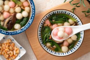 Eating homemade red and white small tangyuan with savory soup and vegetable.