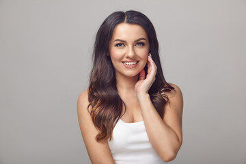 beautiful woman with a clean skin, long hair and sharming smile stands on a grey isolated background