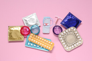 Contraceptive pills, condoms and intrauterine device on pink background, flat lay. Different birth...