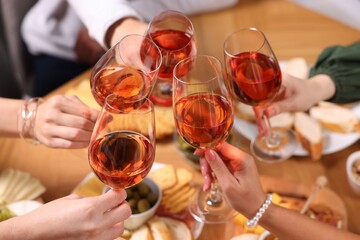 People clinking glasses with rose wine above wooden table, closeup
