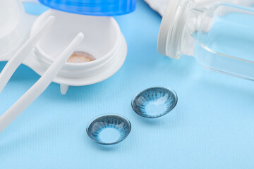 Case with color contact lenses and tweezers on light blue background