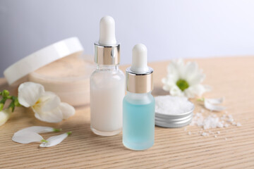 Fototapeta na wymiar Bottles of cosmetic serum and beautiful flowers on wooden table, closeup