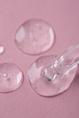 Dripping cosmetic serum from pipette onto pink background, macro view