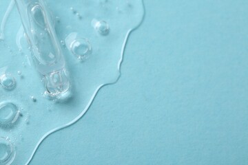 Dripping cosmetic serum from pipette onto light blue background, above view. Space for text