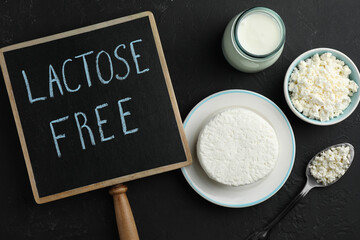 Dairy products and board with phrase Lactose free on black textured table, flat lay