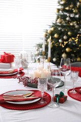 Christmas table setting with burning candles, gift box and dishware indoors