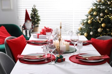 Christmas table setting with burning candles, gift box and dishware indoors
