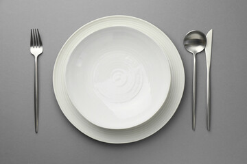 Clean dishes and cutlery on grey background, flat lay