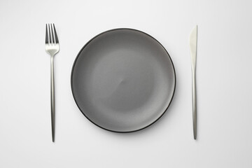 Empty plate, fork and knife on white background, top view