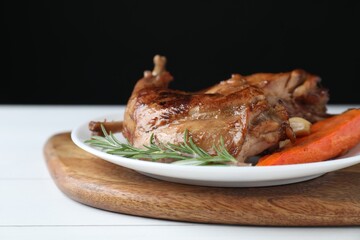 Tasty cooked rabbit meat with rosemary, garlic and carrot on white wooden table, closeup