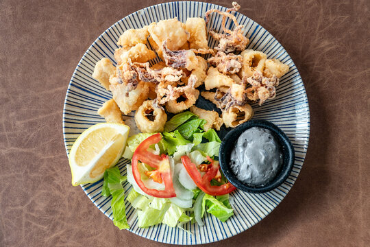 a view over a plate of freshly fried Calamare squid rings served wing squid ink garlic dip.