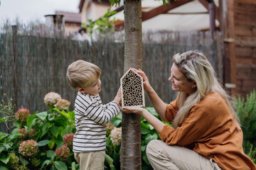 Mother with son making bug hotel, or insect house outdoors in the garden. Boy learning about insects, garden ecosystem and biodiversity.