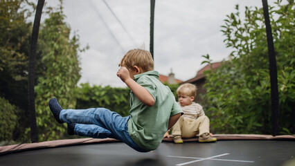 Little boys, brothers jumping on trampoline in the backyard, doing somersaults. Dangers and risks of trampoline for kids.