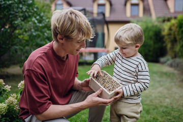Father with little boy making bug hotel, or insect house outdoors in the garden. Boy learning about...