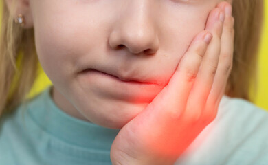 A little girl holds her hand on her sore cheek and has a toothache. The concept of malocclusion in...