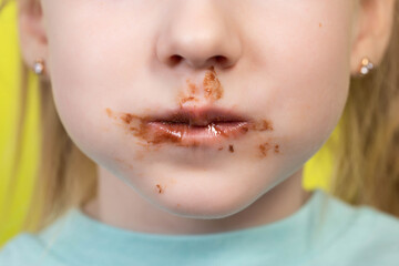 Little girl's mouth dirty with chocolate on a yellow background. Concept of children with a sweet...