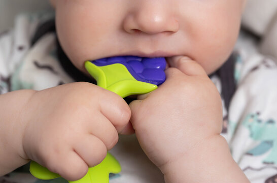 A child holds a rubber toy massager for teething in his hand. Itching and salivation from the mouth. First teeth. Help with teething, close-up