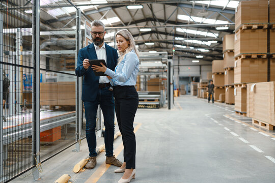 Female engineer and male production manager standing in modern industrial factory, talking about production. Manufacturing facility with robotics and automation.
