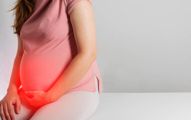 A pregnant girl holds her red lower belly on a gray background. The concept of depression and...
