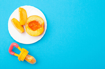 Nibbler for children and a plate with peach on a blue background. Chewing reflex concept and treat...