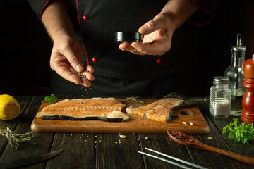 The chef adds coriander to the fish steak before salting it. Concept of preparing a fish dish on a kitchen table in a restaurant